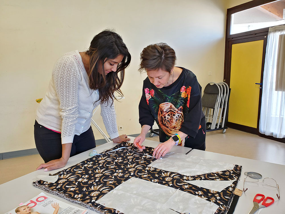 Deux femmes en train de faire de la couture autour d'une table sur laquelle il y a du tissu sombre